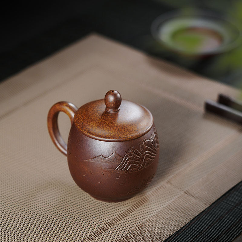 Handmade Yixing purple sand tea cup with lid, featuring mountain design, perfect for enjoying tea.