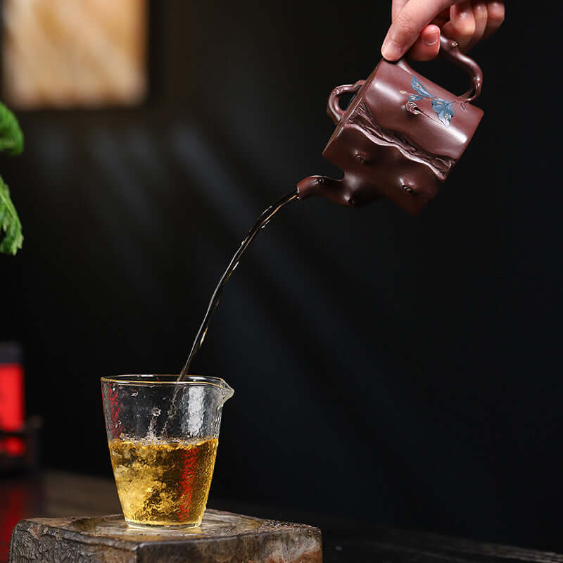 Handmade Yixing purple sand teapot pouring tea into a glass, showcasing traditional craftsmanship and tea culture.