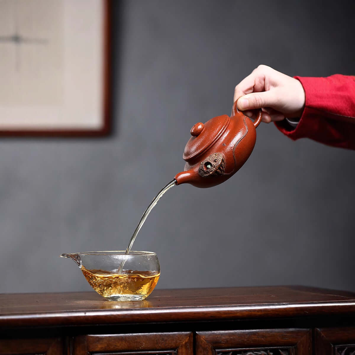 Handmade Yixing purple sand teapot pouring tea into a glass cup on a wooden table, showcasing traditional kung fu tea set.