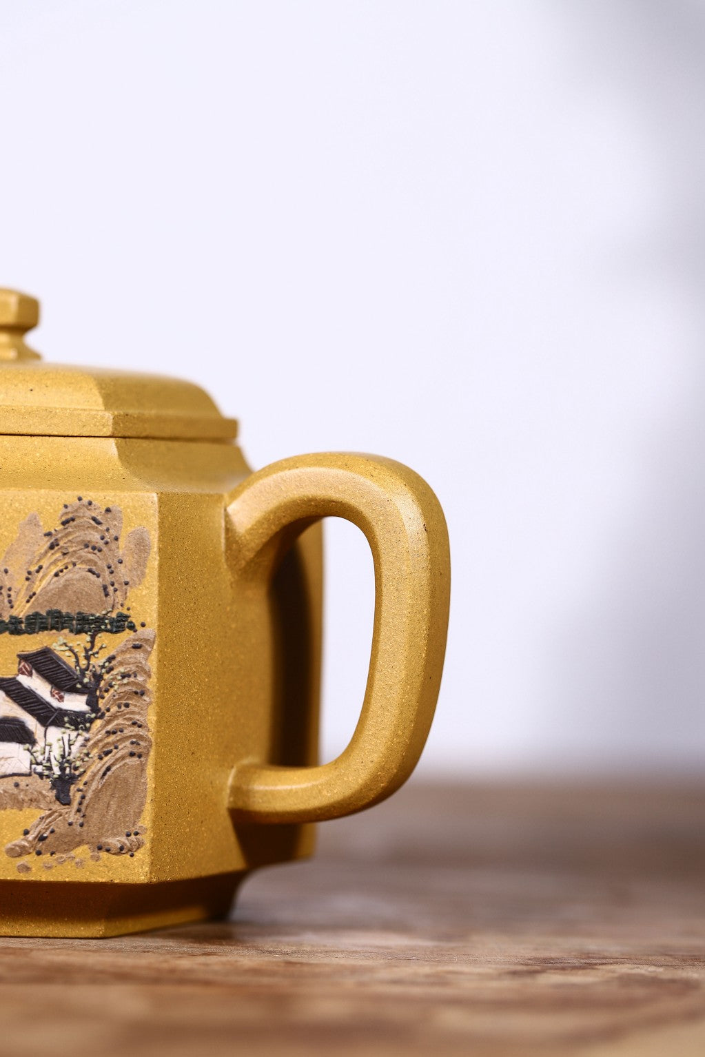 Handmade Yixing purple sand teapot with intricate mountain scenery design in golden clay, showcasing fine craftsmanship.