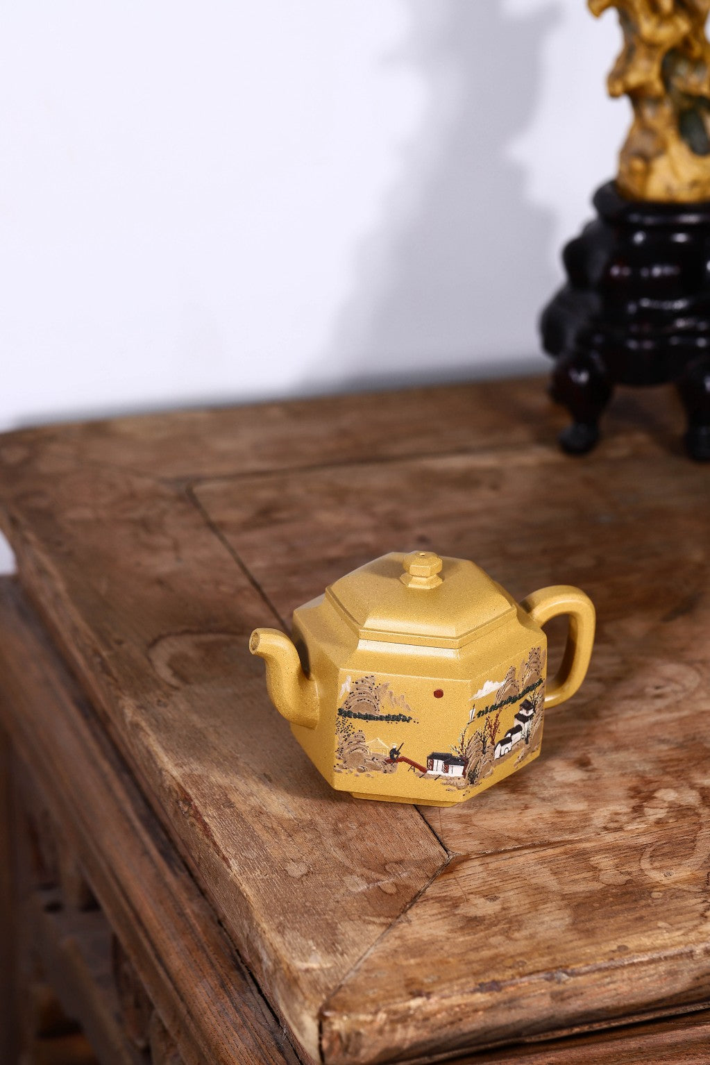 Handmade Yixing purple sand teapot in hexagonal shape with landscape design on wooden table.