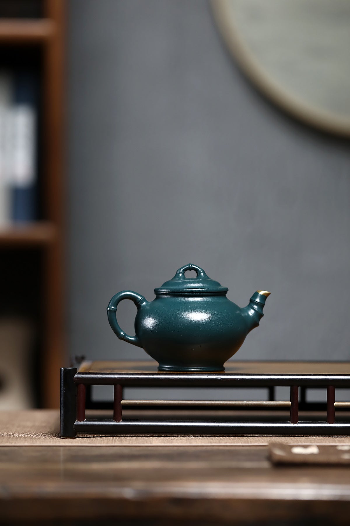 Handmade Yixing purple sand teapot in dark green, elegantly displayed on a wooden stand.