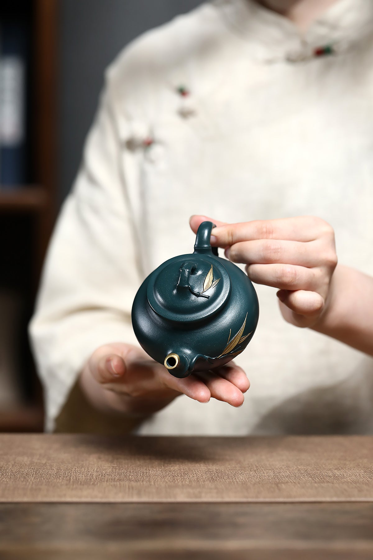 Handmade Yixing purple sand teapot in green hue, displayed by a person wearing traditional attire, showcasing its unique design.