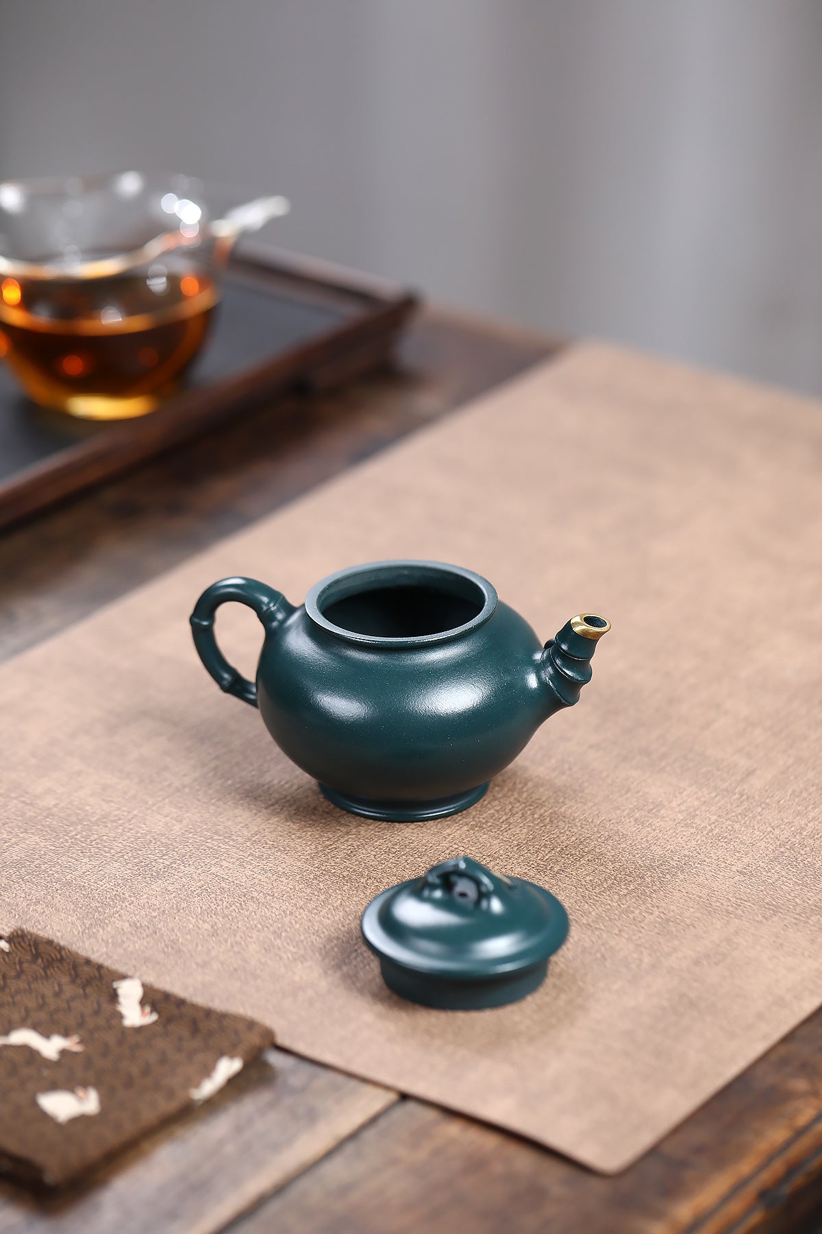 Handmade Yixing purple sand teapot in deep green color, with bamboo-inspired design, displayed on a textured table.