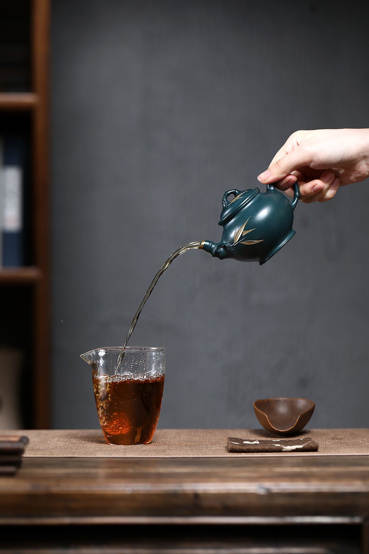Handmade Yixing purple sand teapot pouring tea into a glass measuring cup, showcasing rich color and craftsmanship.