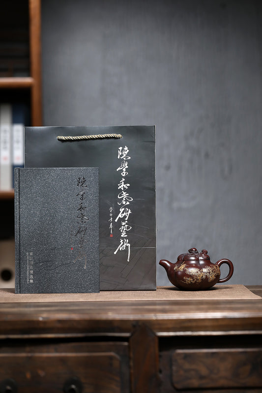 Handmade Yixing purple sand teapot with accompanying book and elegant packaging on a wooden surface.
