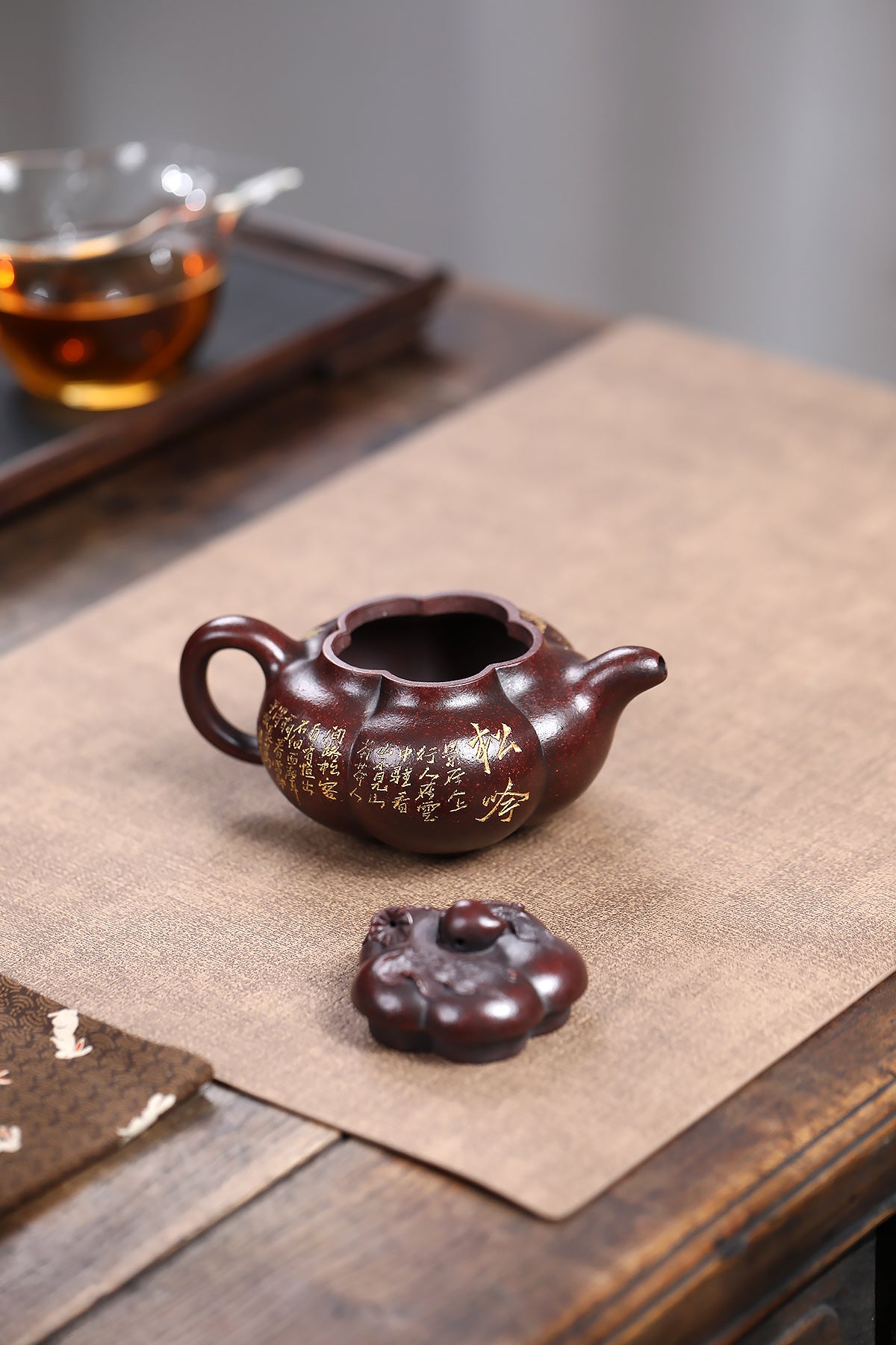 Handmade Yixing purple sand teapot with gold inscriptions, accompanied by lid, displayed on wooden table.
