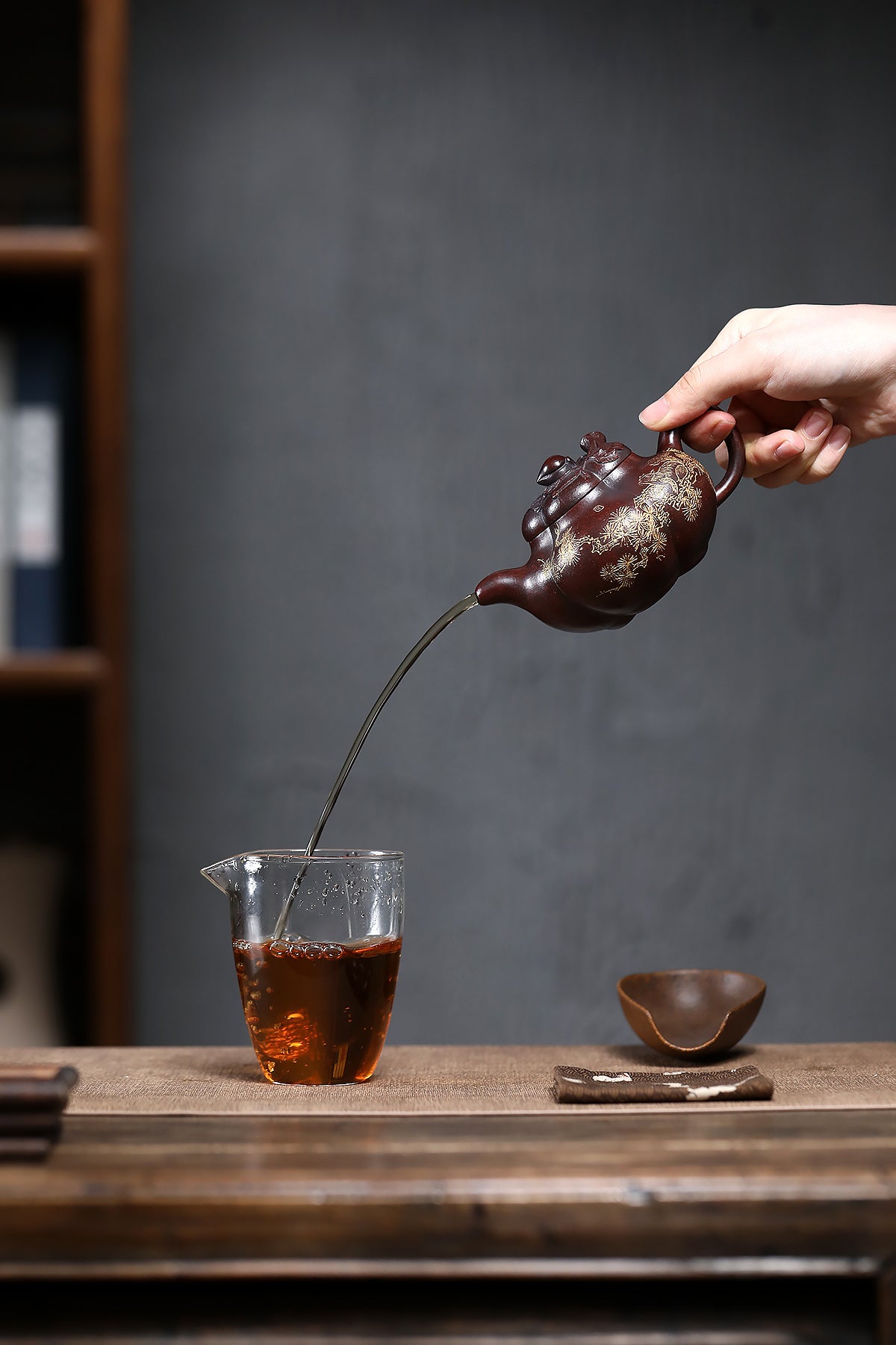 Handmade Yixing purple sand teapot pouring tea into glass cup, showcasing traditional craftsmanship and elegance.
