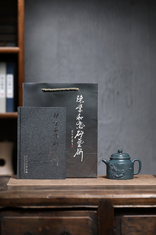 Handmade Yixing purple sand teapot displayed with an elegant gift box and book on a wooden table background.