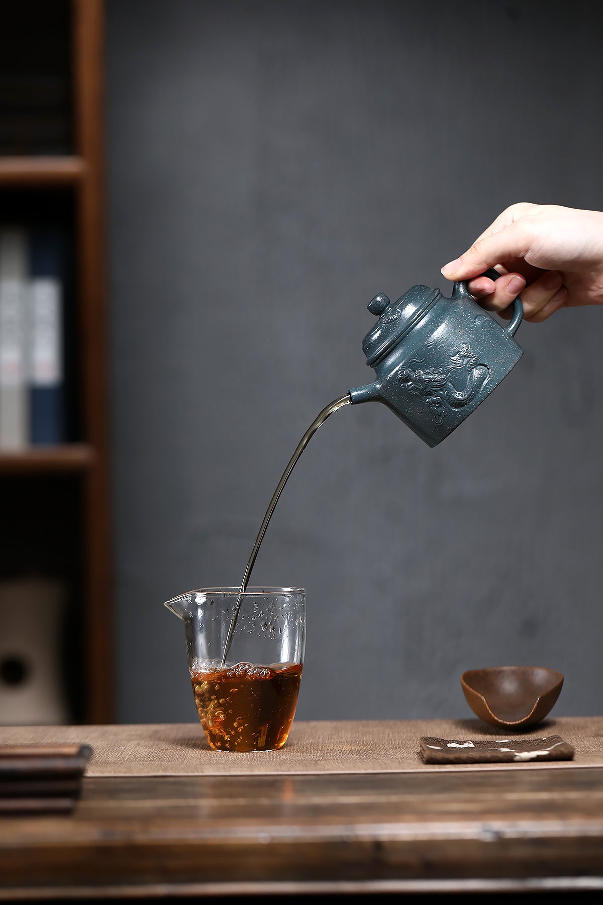 Handmade Yixing purple sand teapot pouring tea into a glass cup, showcasing traditional craftsmanship and unique design.