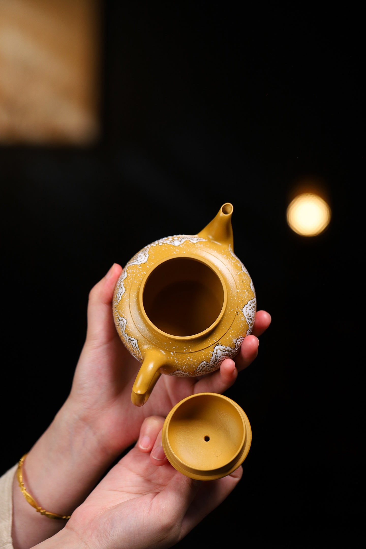 Handmade Yixing purple sand teapot with intricate design, held by a person against a dark background.