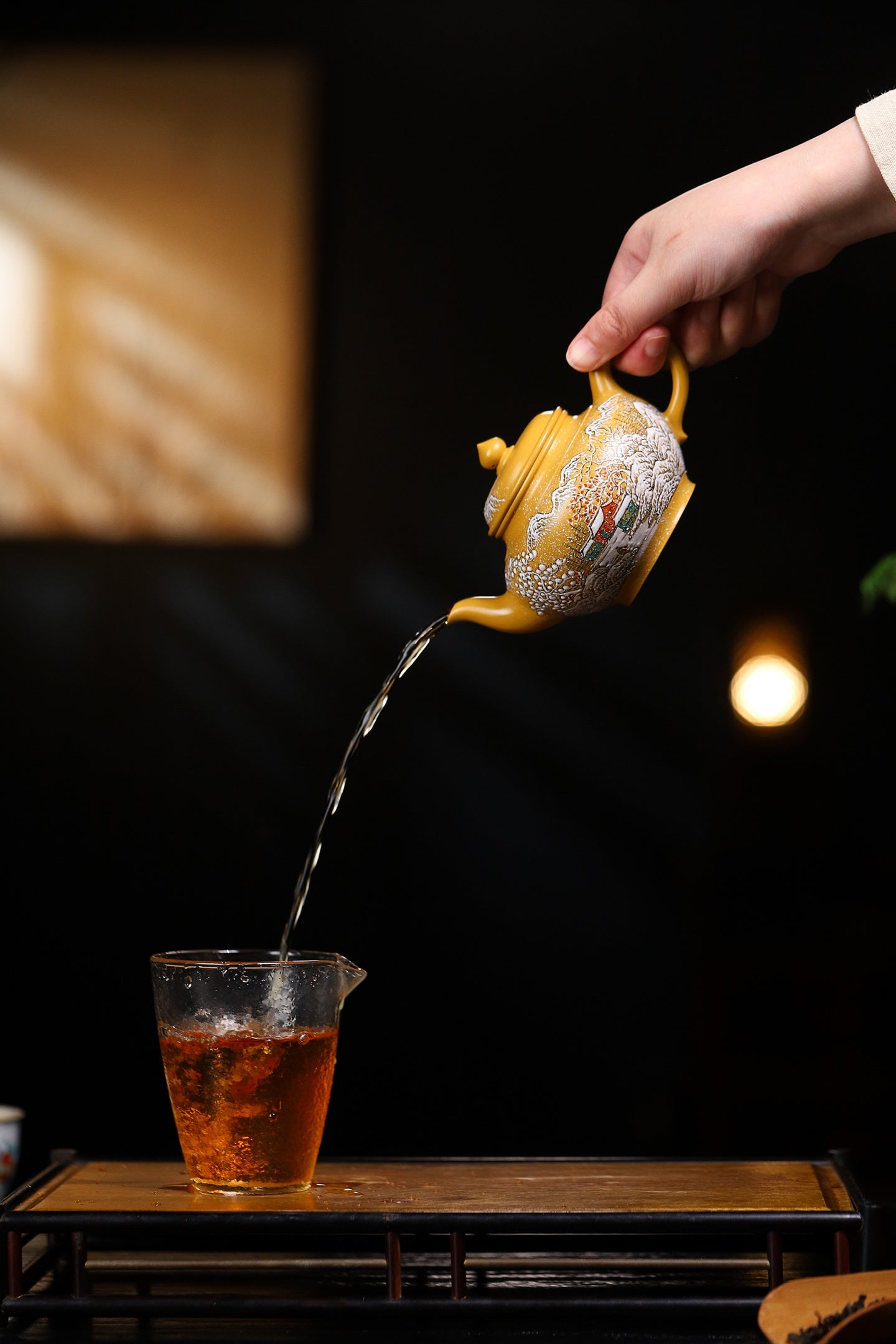Hand pouring tea from a handcrafted Yixing purple sand teapot into a glass cup, showcasing traditional tea ceremony.