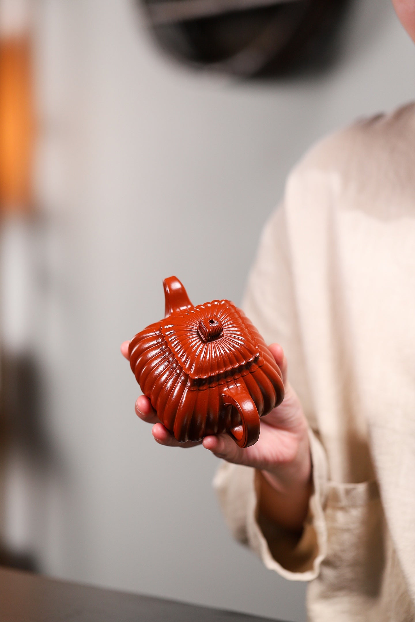 Handmade Yixing purple sand teapot with intricate design, held by a person in a soft-toned garment.