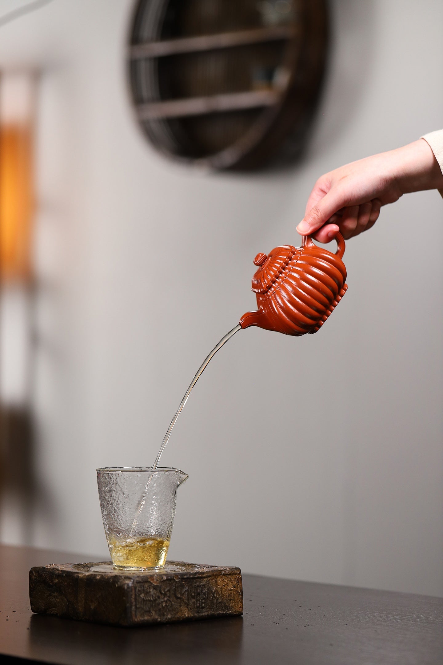 Handmade Yixing purple sand teapot pouring tea into a glass cup on a wooden table, showcasing elegant craftmanship.