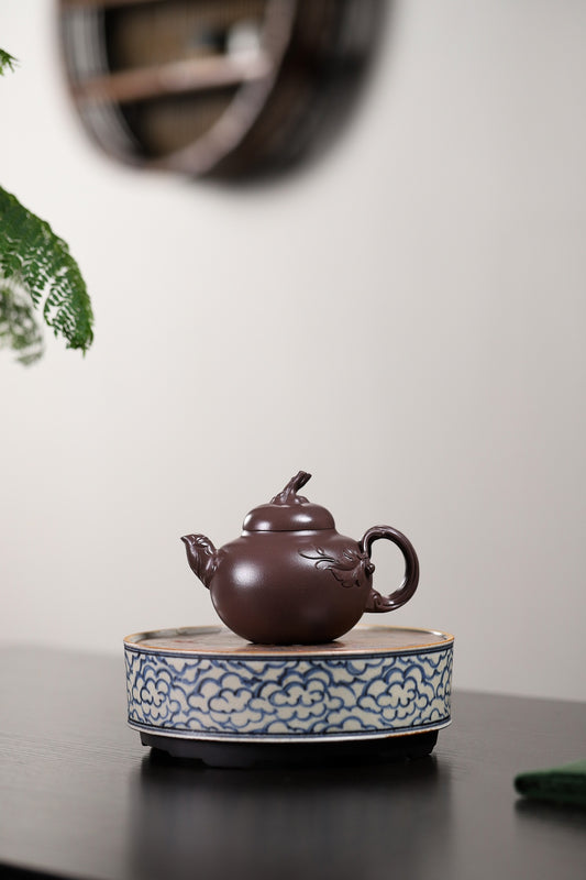 Handmade Yixing purple sand teapot displayed on a decorative plate with a natural background.