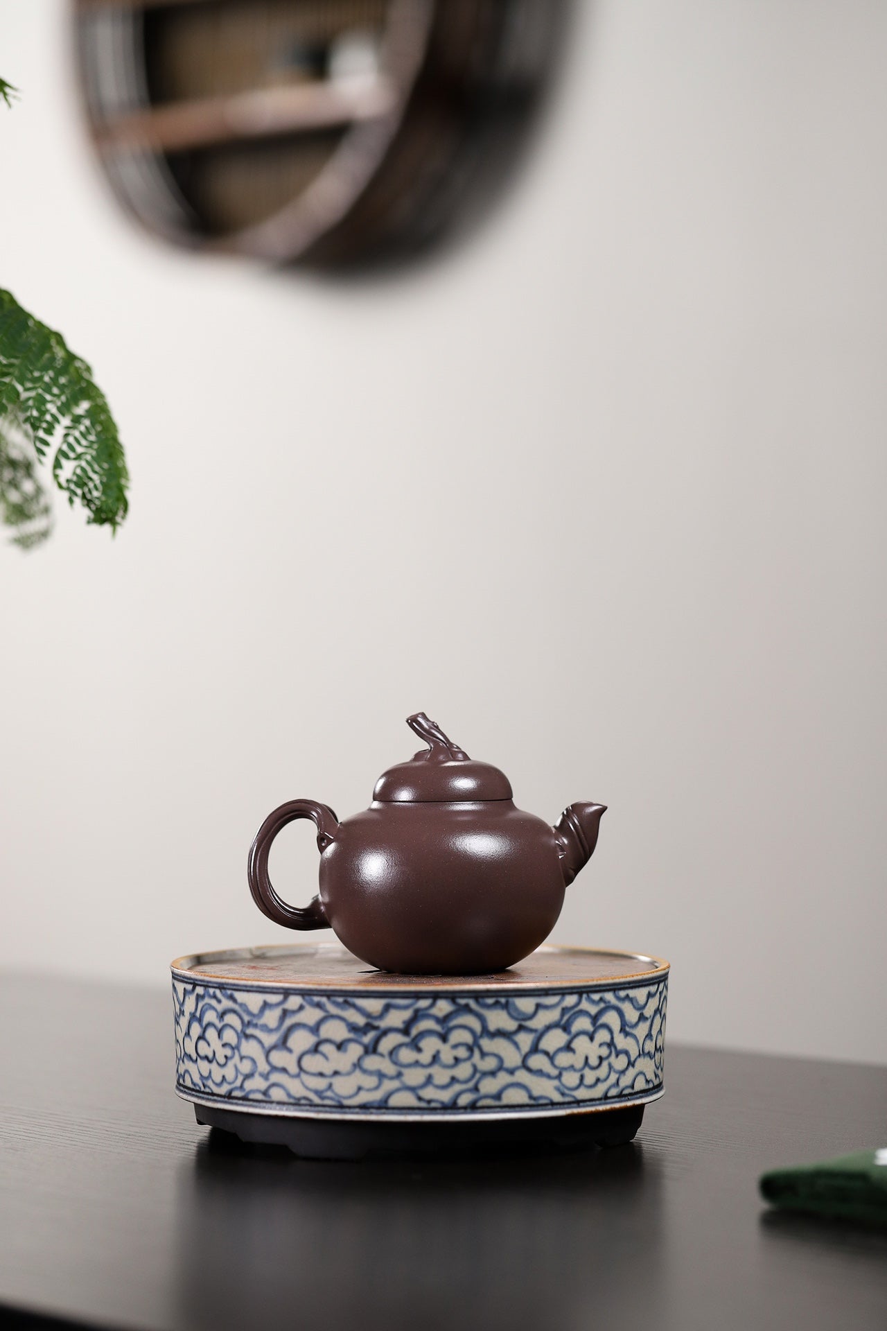 Handmade Yixing purple sand teapot displayed on a decorative stand with blue cloud patterns, showcasing traditional craftsmanship.