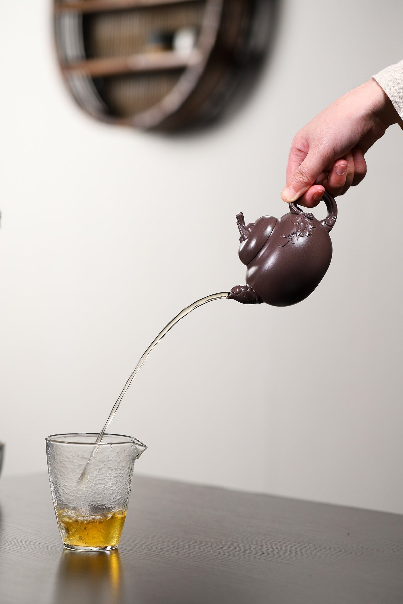 Handmade Yixing purple sand teapot pouring tea into a glass cup, showcasing elegant craftsmanship and design.