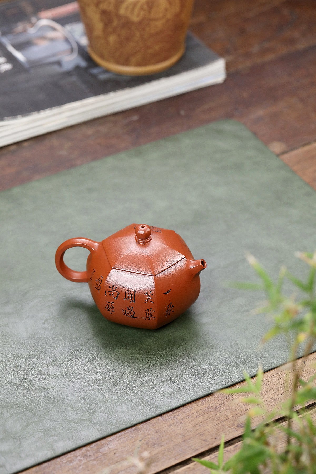 Handmade Yixing purple sand teapot with calligraphy design on a textured green mat.