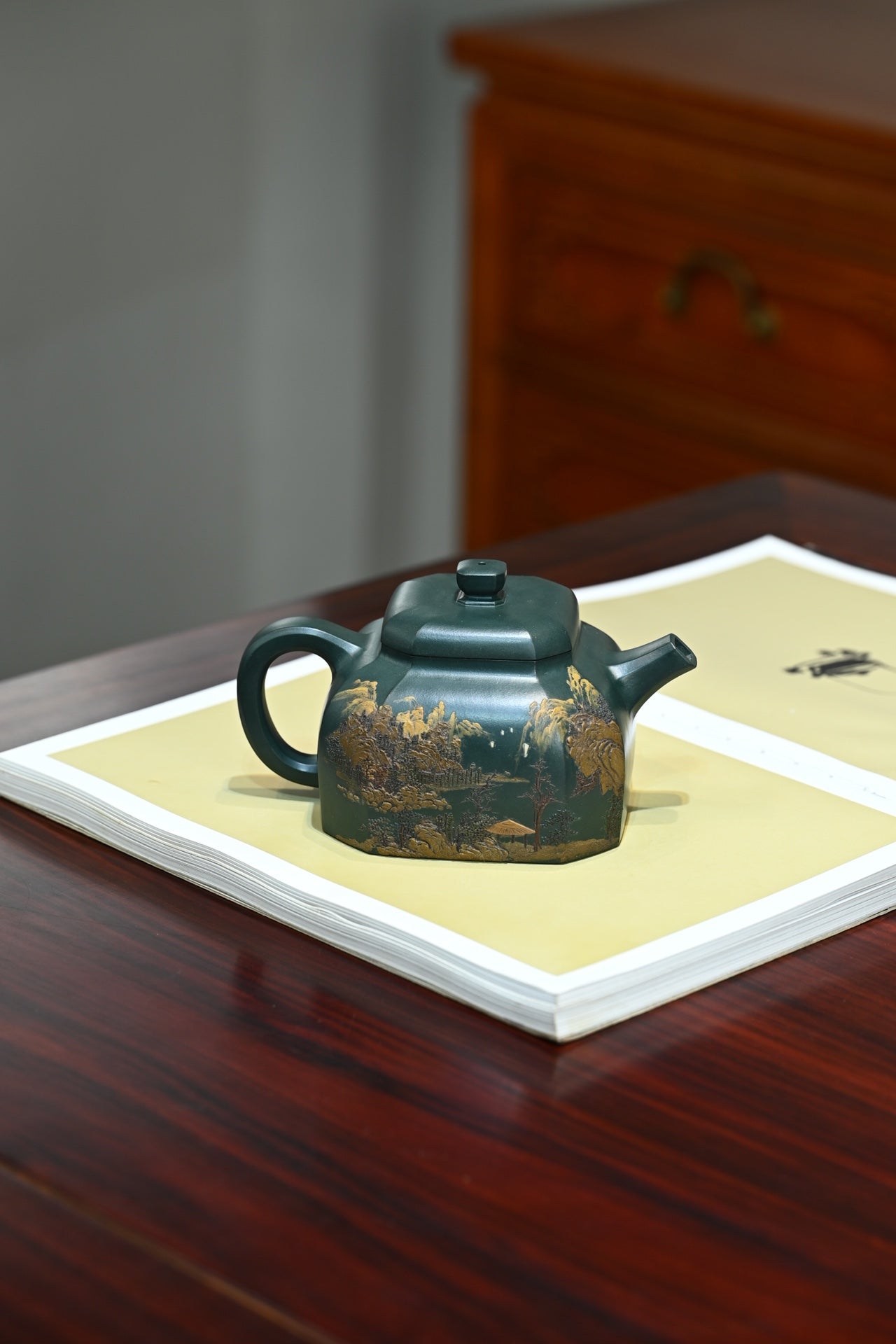 Handmade Yixing purple sand teapot with intricate mountain scene design on a table with art paper.