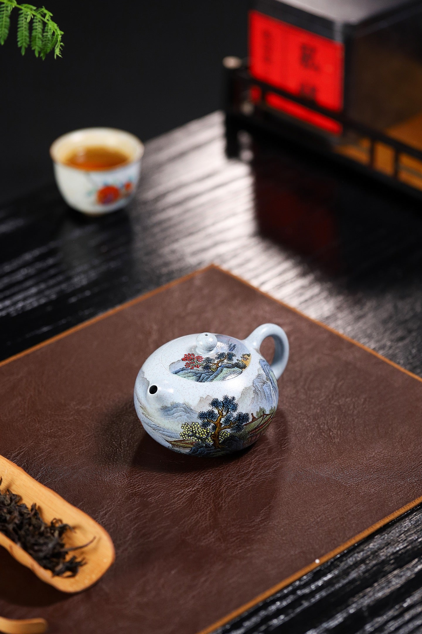 Handmade Yixing purple sand teapot with floral design, placed on a dark wooden surface beside a tea cup.