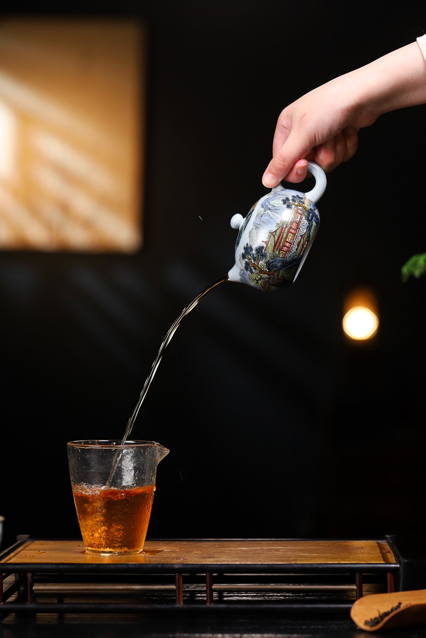 Hand pouring tea from a decorative teapot into a glass cup, showcasing the elegance of tea preparation.