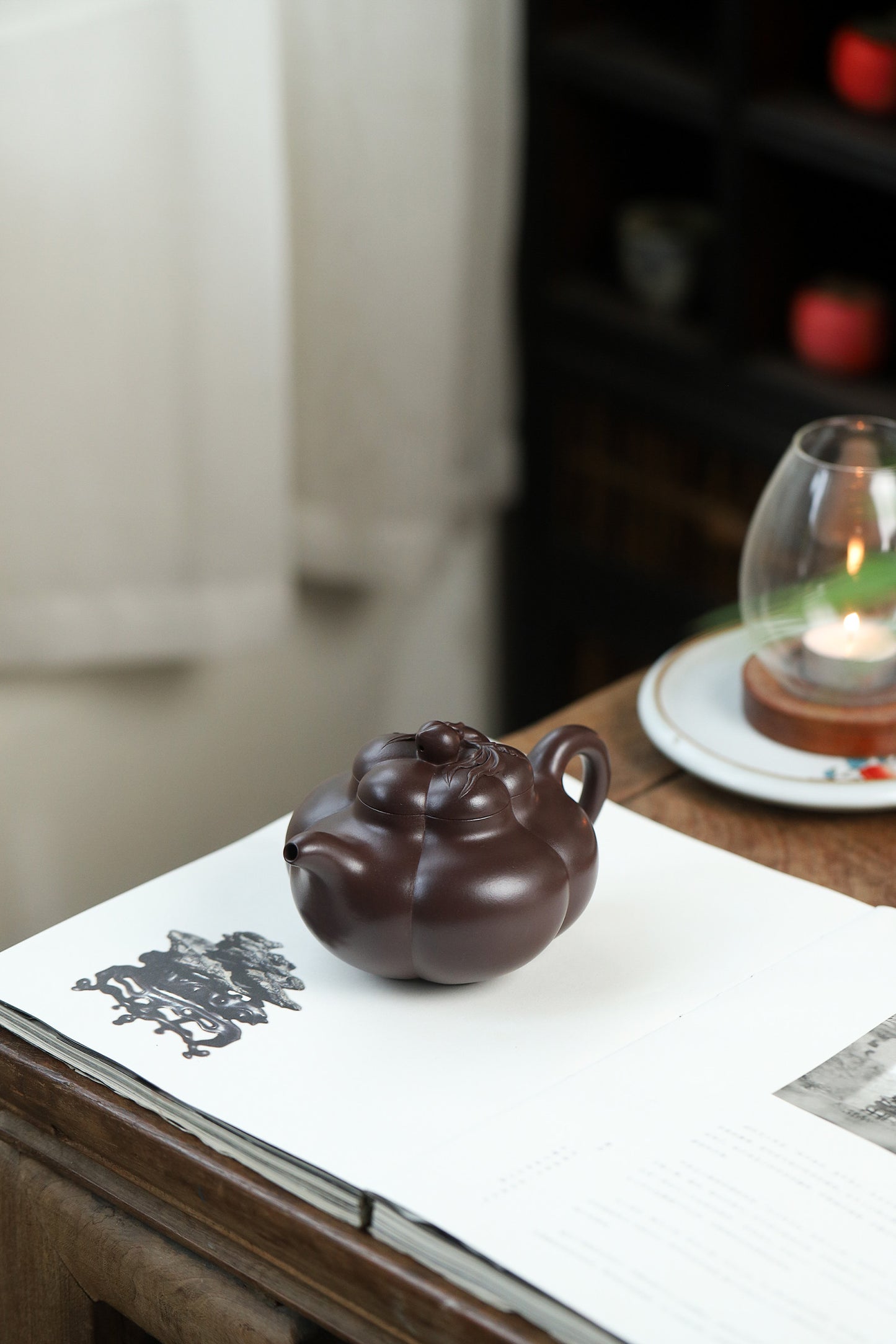 Handmade Yixing purple sand teapot, featuring a unique peach design, displayed on a wooden table with a candle.