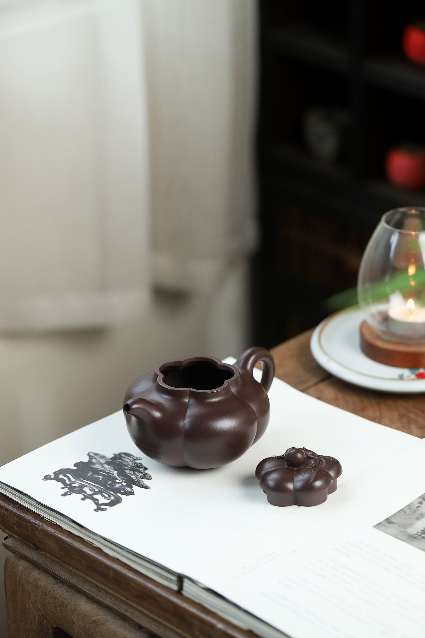 Handmade Yixing purple sand teapot with a pumpkin shape, displayed on a table with a candle.