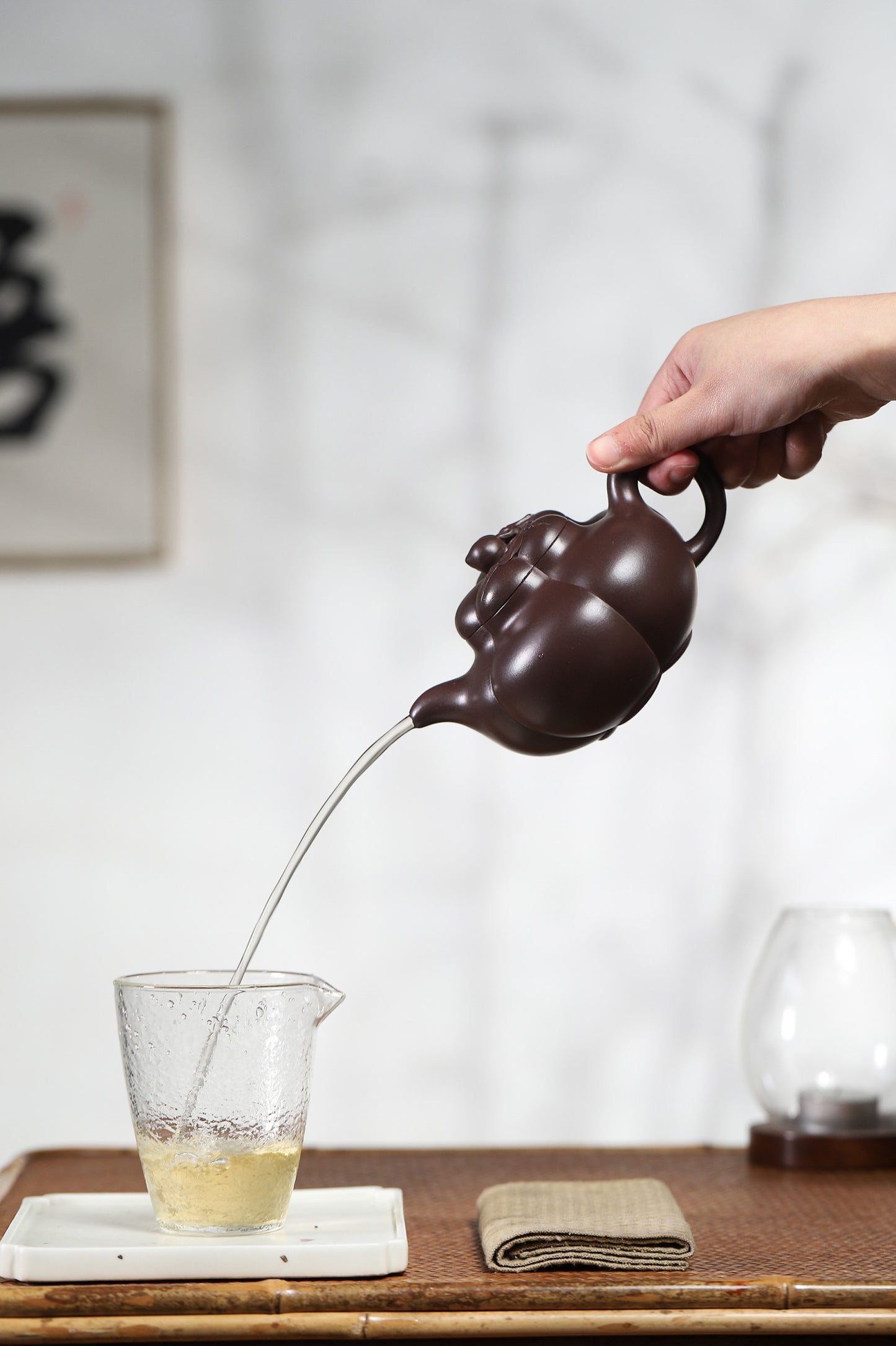 Handmade Yixing purple sand teapot pouring tea into glass, showcasing its elegant design and craftsmanship.