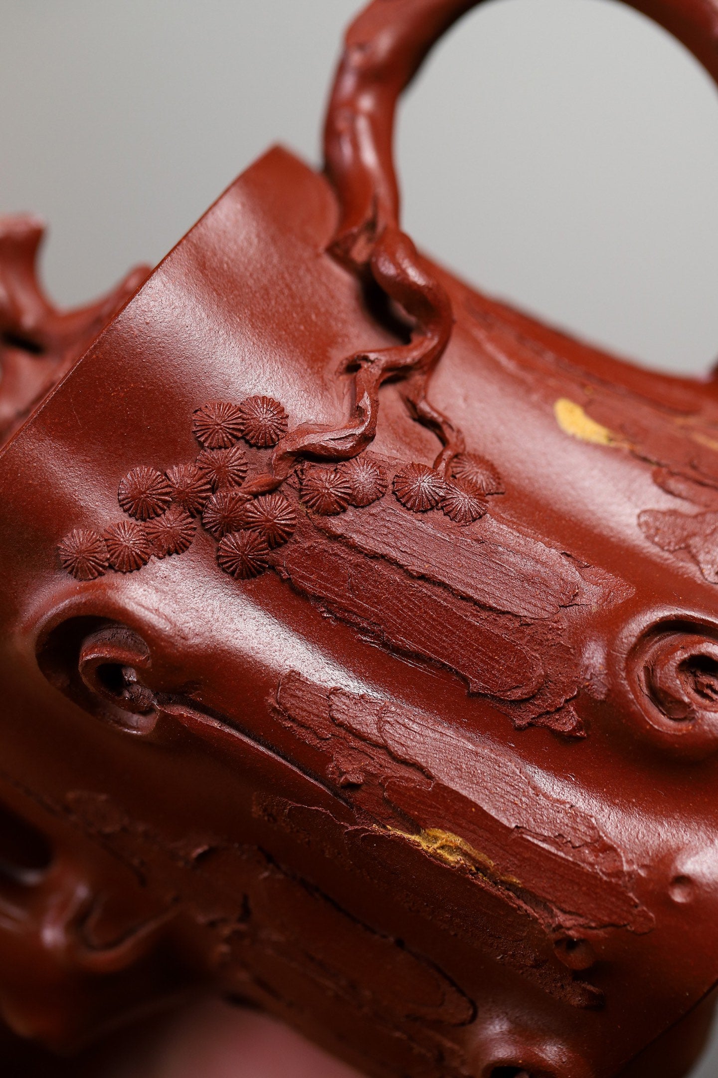 Close-up of a handmade Yixing purple sand teapot featuring intricate branch and flower detailing.