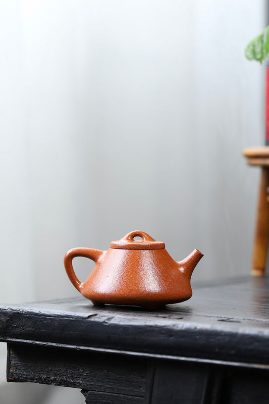 Handmade Yixing purple sand teapot on a black wooden table, showcasing unique craftsmanship and warm colors.
