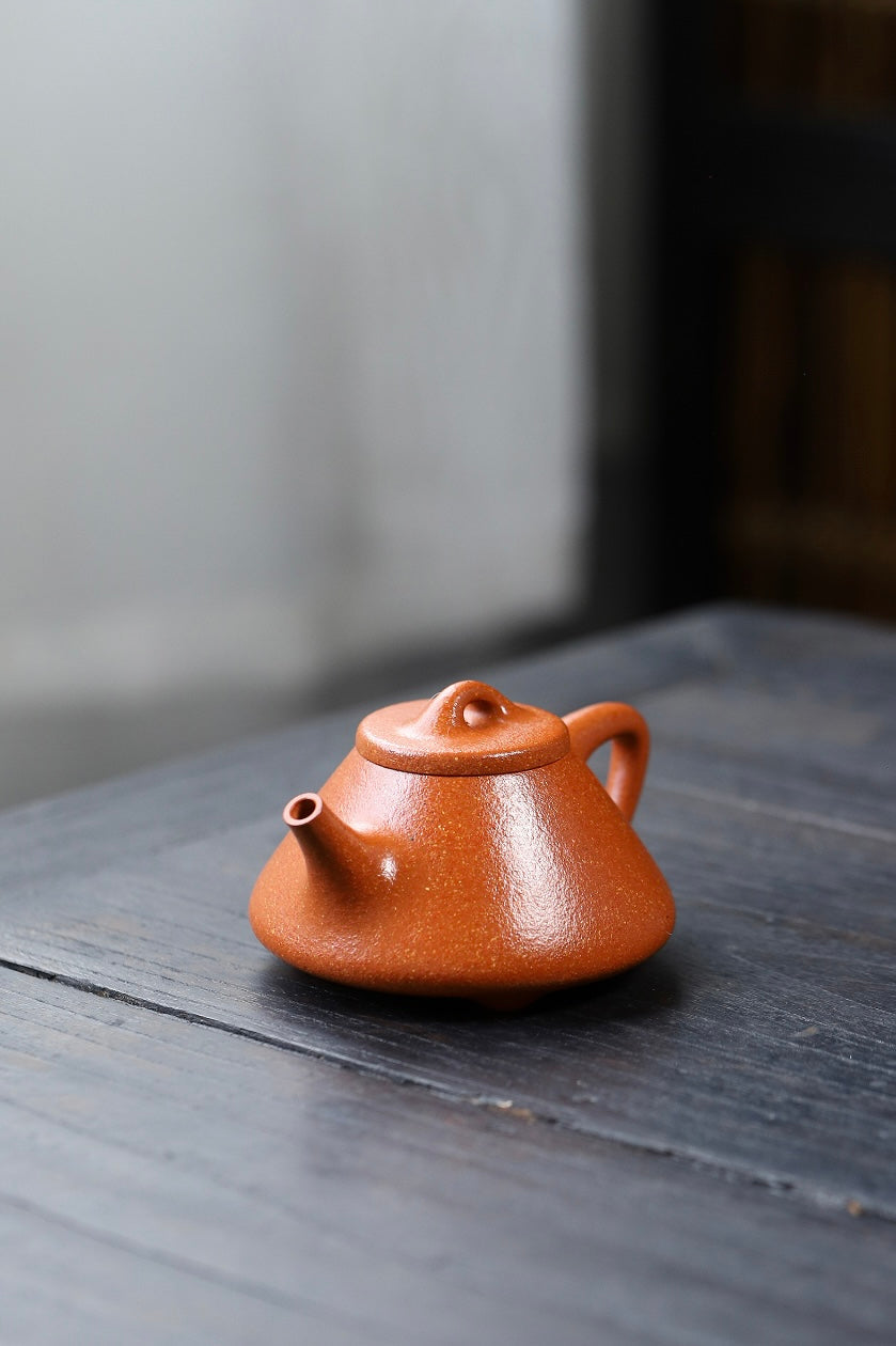Handmade Yixing purple sand teapot on wooden table, showcasing a unique orange hue and traditional design.