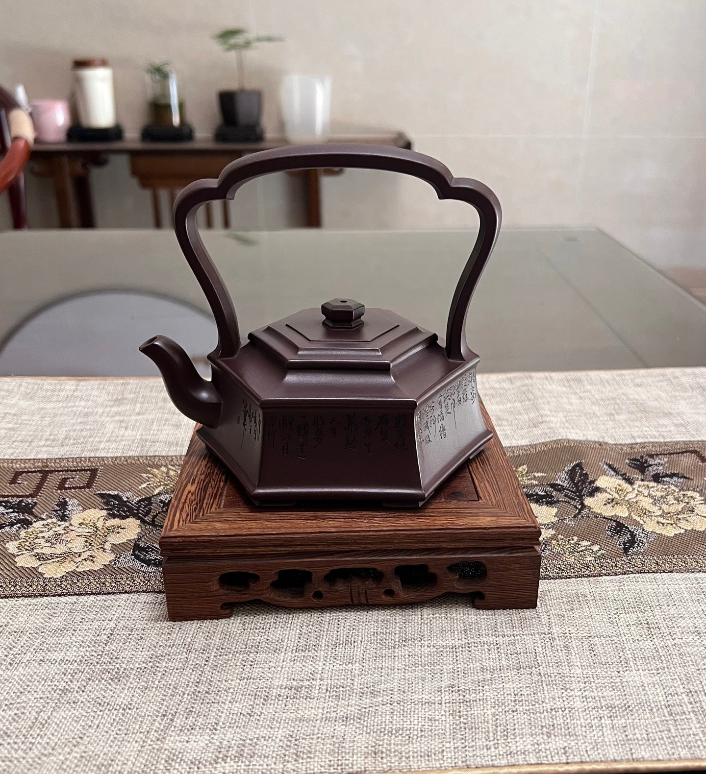 Handmade Yixing purple sand teapot with hexagonal design and a raised handle, displayed on a wooden stand.