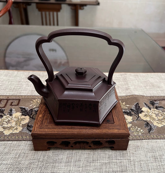 Handmade Yixing purple sand teapot with a hexagonal body and ornate handle, showcased on a wooden base.