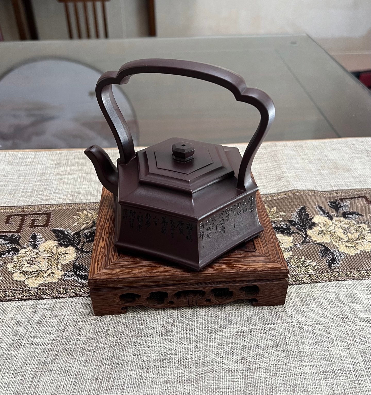Handmade Yixing purple sand teapot with hexagonal base and elegant handle, displayed on a wooden stand.