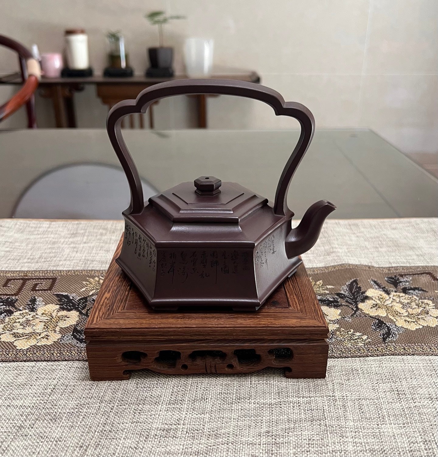 Handmade Yixing purple sand teapot with hexagonal design and prominent handle, displayed on a wooden stand.