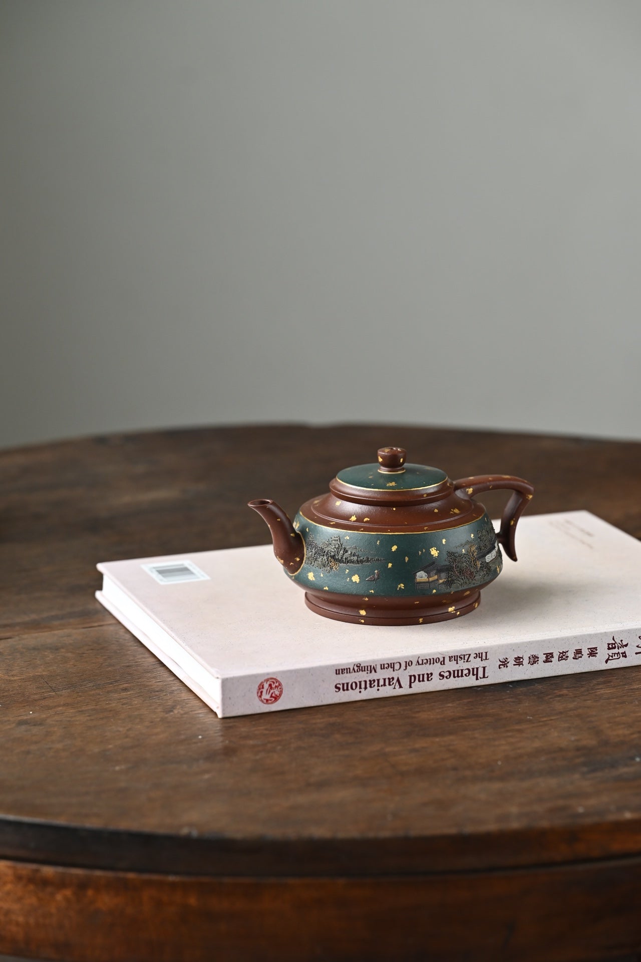 Handmade Yixing purple sand teapot resting on a book, showcasing elegant craftsmanship and unique design.