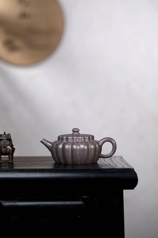 Handmade Yixing purple sand teapot on a wooden table, showcasing its unique pumpkin shape and craftsmanship.