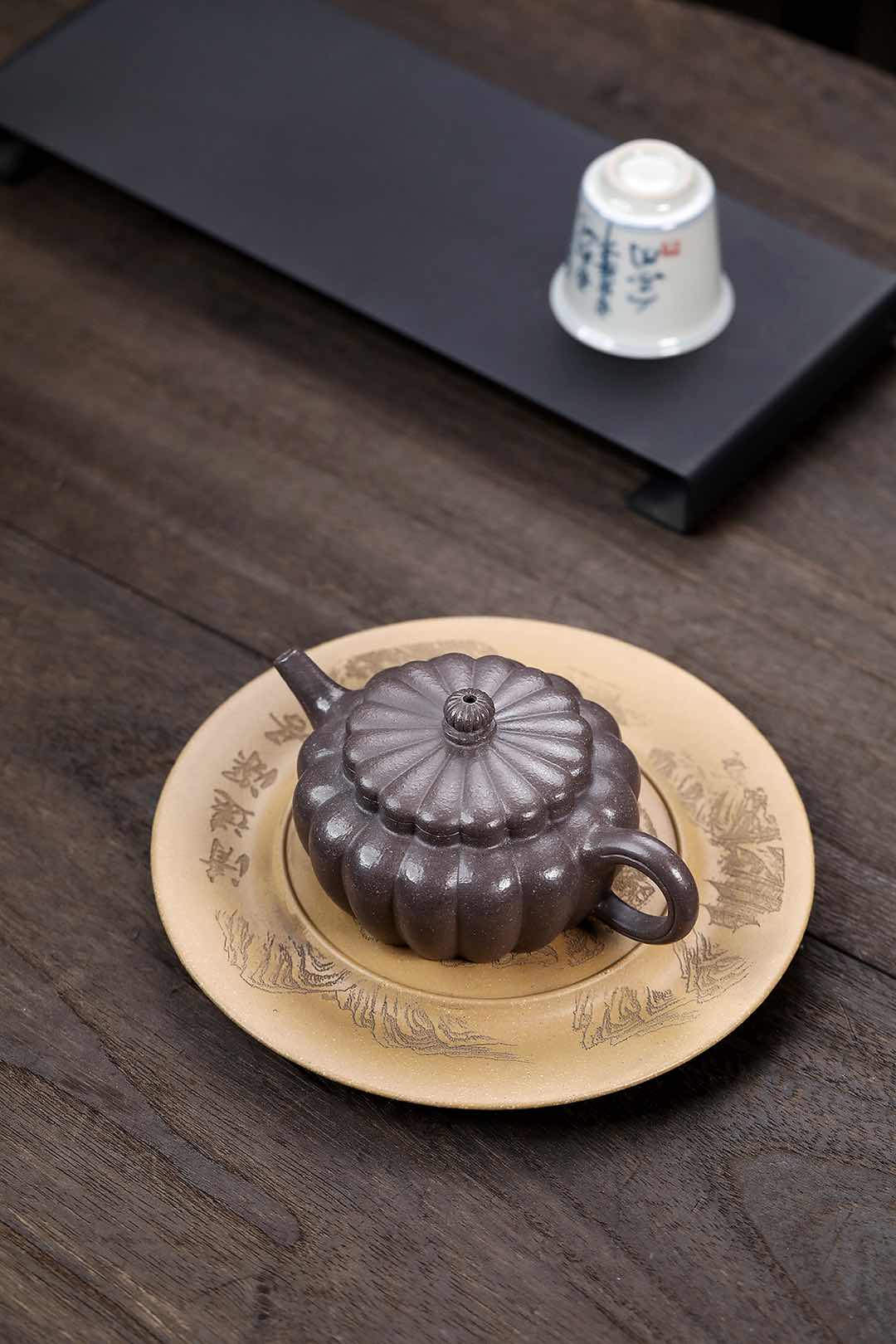 Handmade Yixing purple sand teapot in a floral plate on a wooden table, showcasing elegant design and craftsmanship.