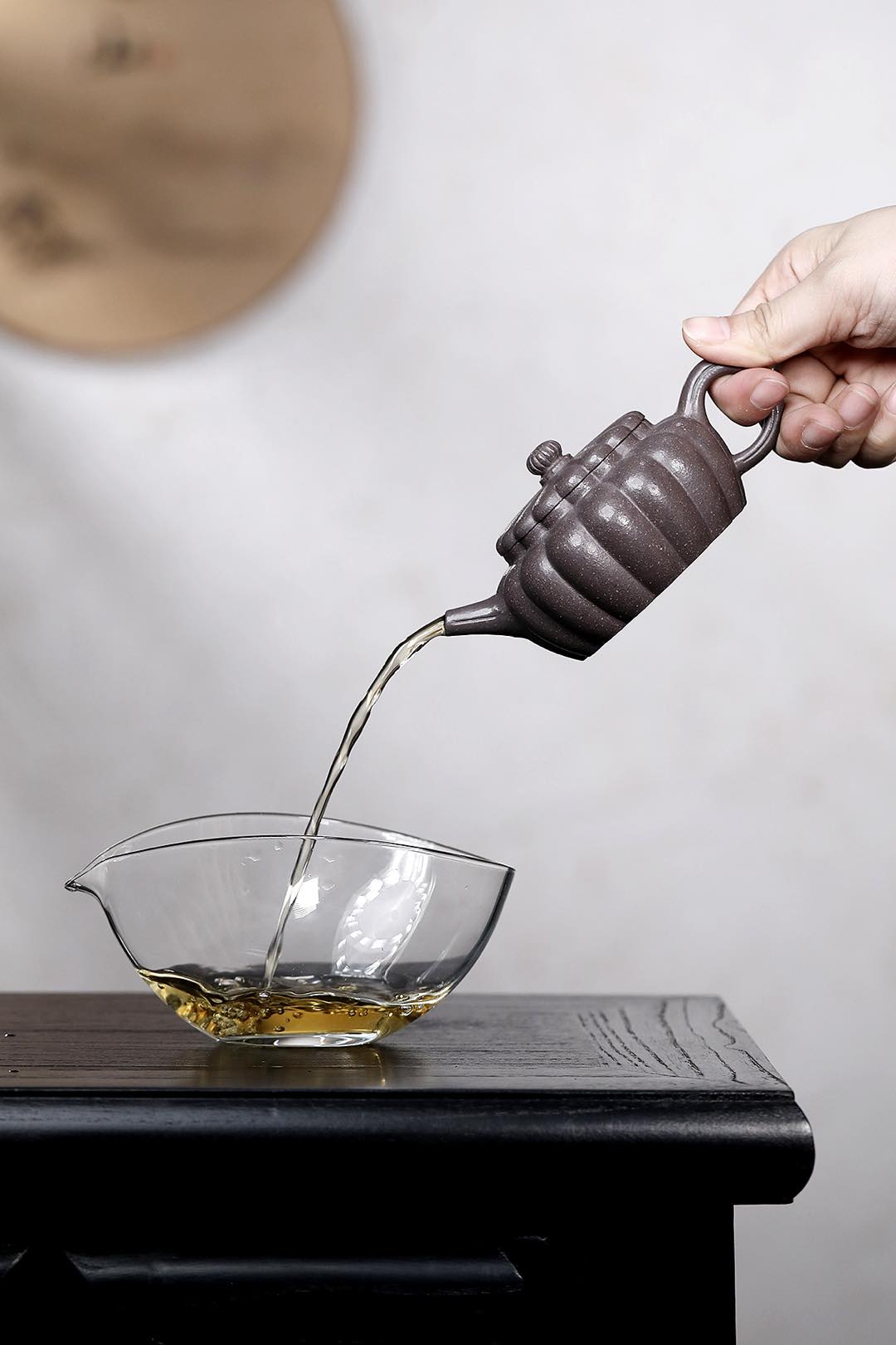Handmade Yixing purple sand teapot pouring tea into a glass vessel on a dark wood table.
