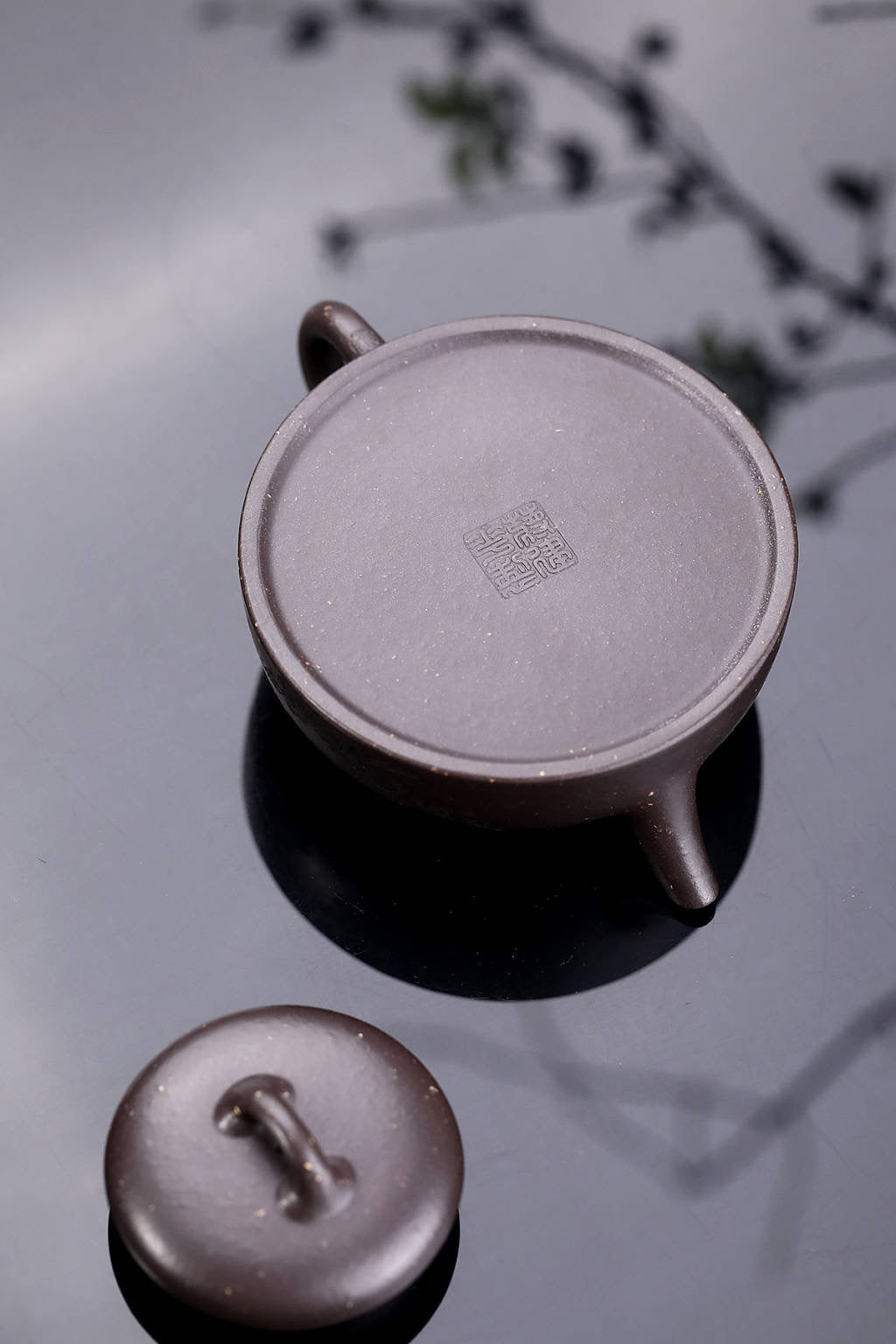 Handmade Yixing purple sand teapot lid and base on reflective surface, showcasing artisan craftsmanship.