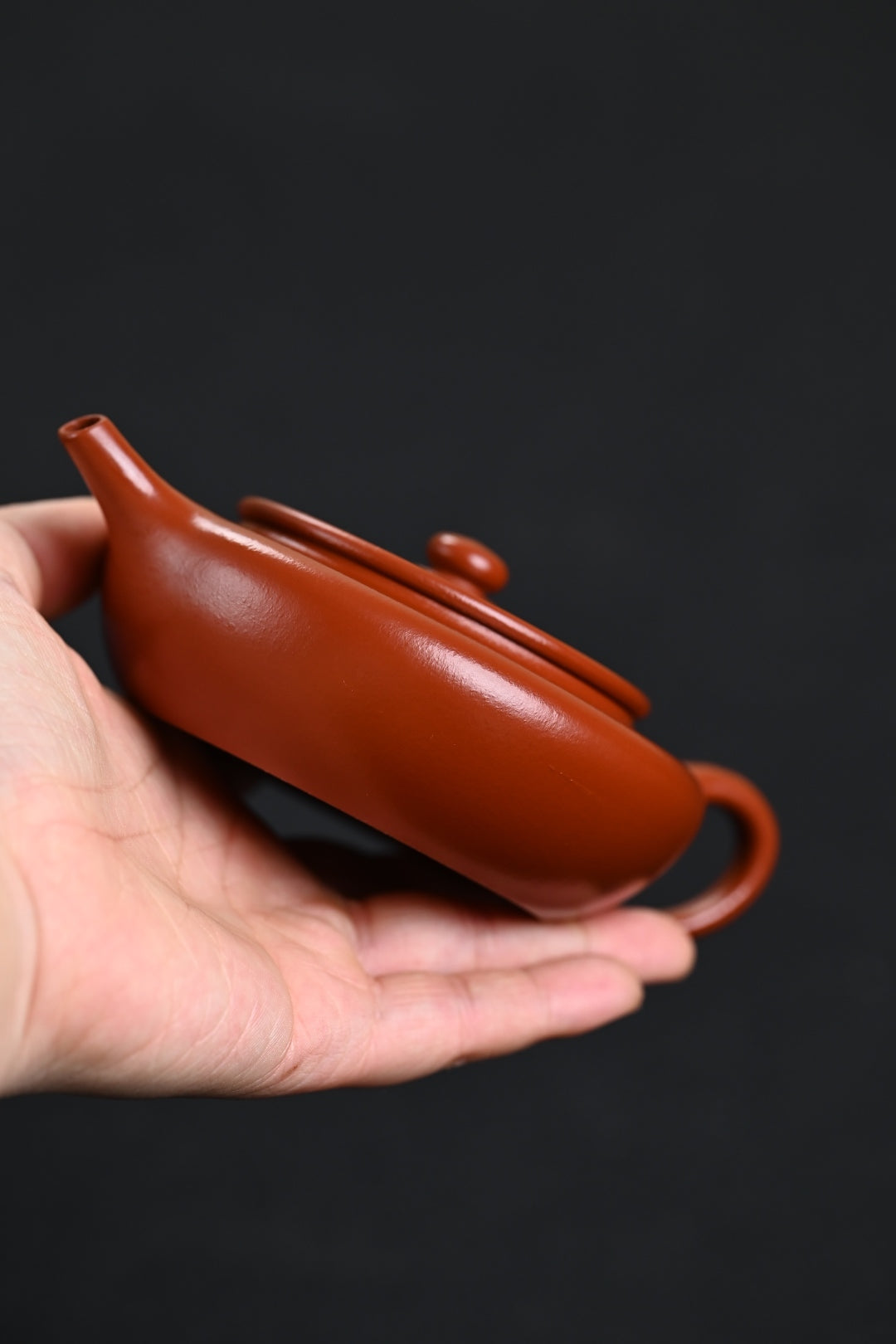 Handmade Yixing purple sand teapot in hand, showcasing unique design and craftsmanship.