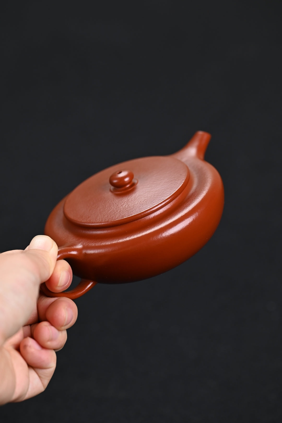 Handmade Yixing purple sand teapot in hand, showcasing its elegant design and rich mahogany color.