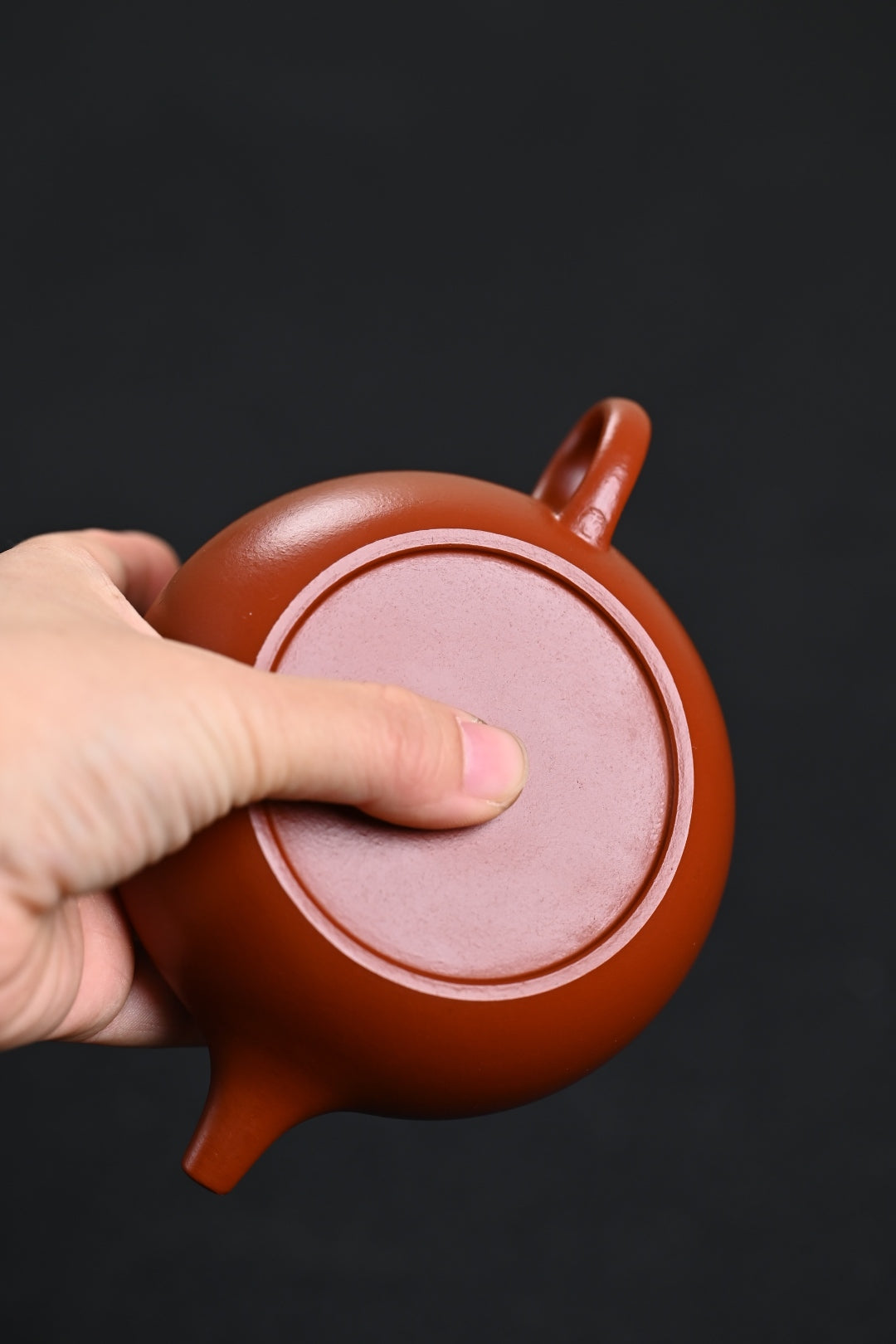 Handmade Yixing purple sand teapot with unique design, held in hand against a black background.