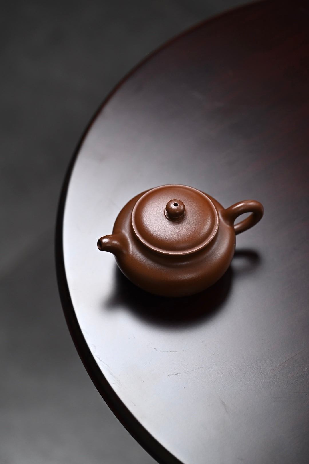 Handmade Yixing purple sand teapot on a dark wooden table, showcasing fine craftsmanship and elegant design.