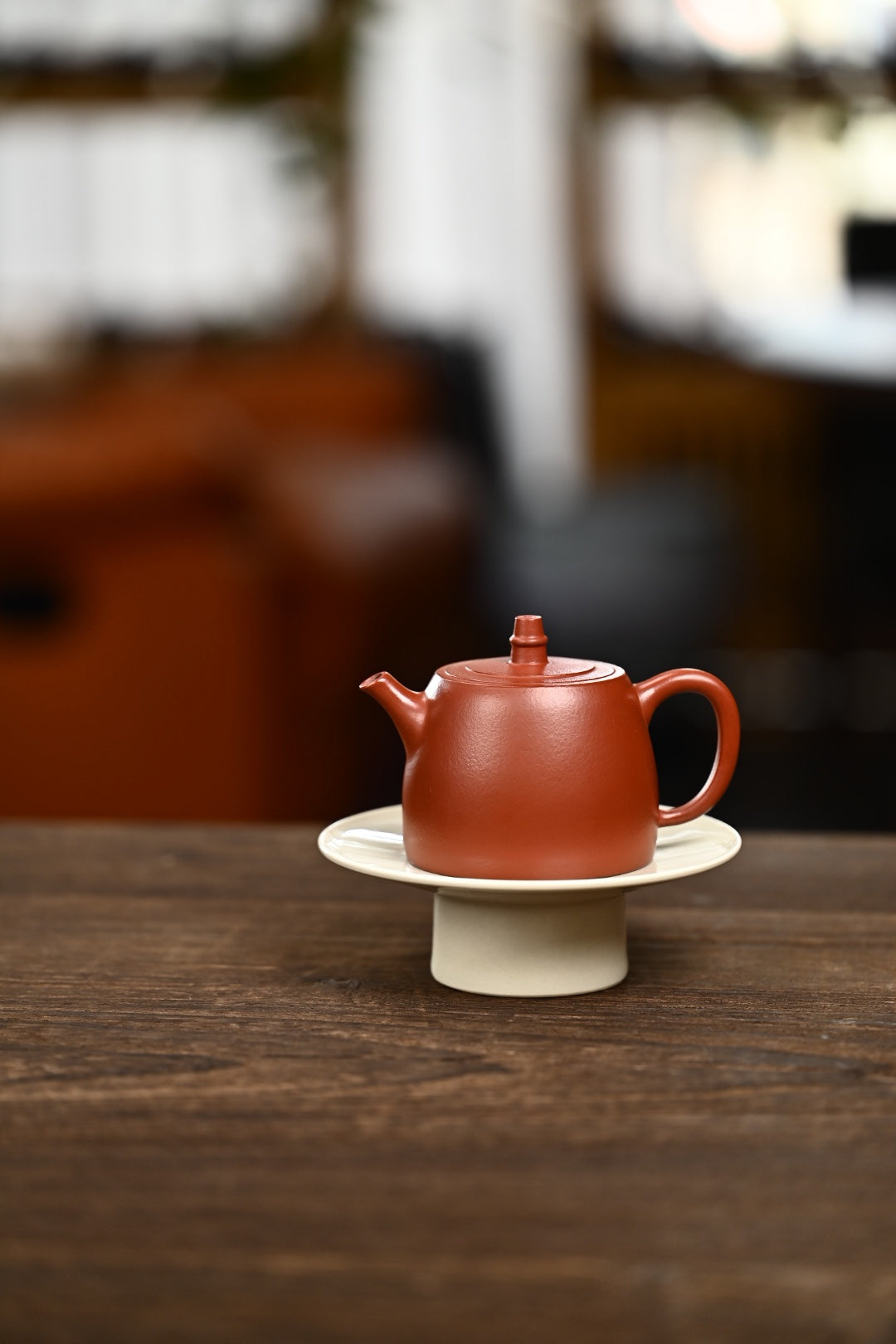 Handmade Yixing purple sand teapot on a white saucer, featuring rich red clay and a traditional design.