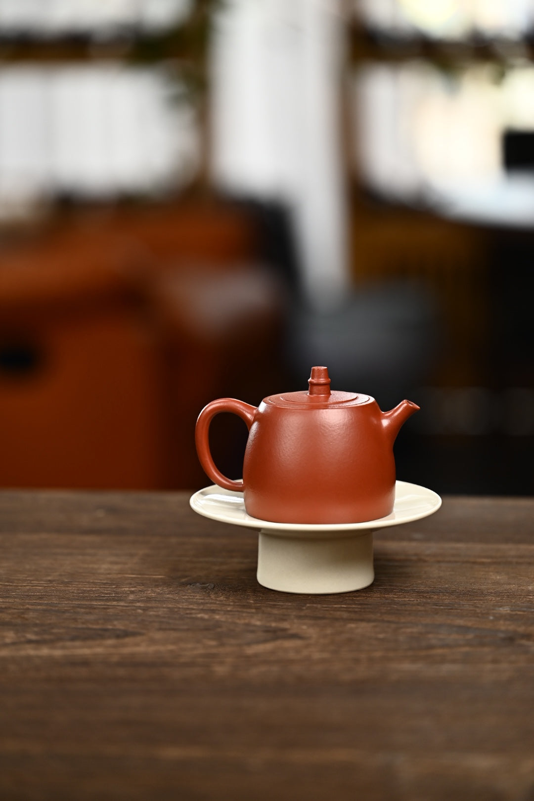 Handmade Yixing purple sand teapot on a plate, showcasing a rich red hue and elegant design.