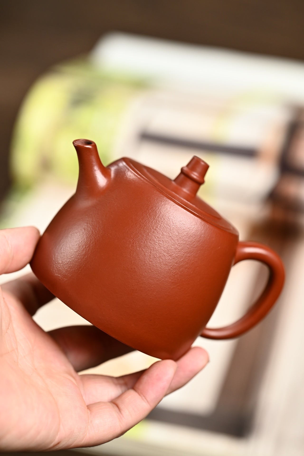 Handmade Yixing purple sand teapot held in hand, showcasing its smooth, rich red clay surface.
