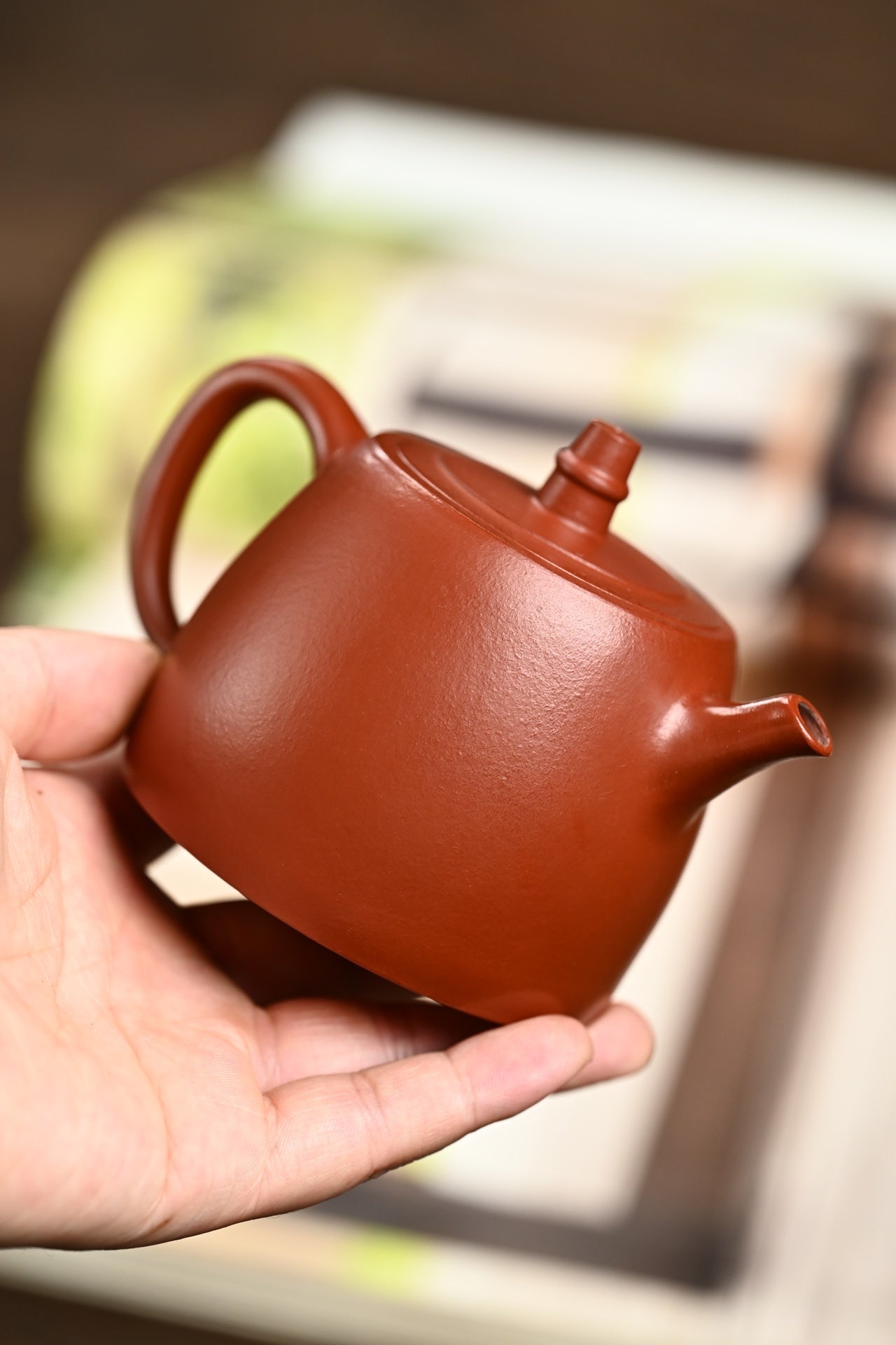 Handmade Yixing purple sand teapot held in hand, showcasing its elegant design and rich color.