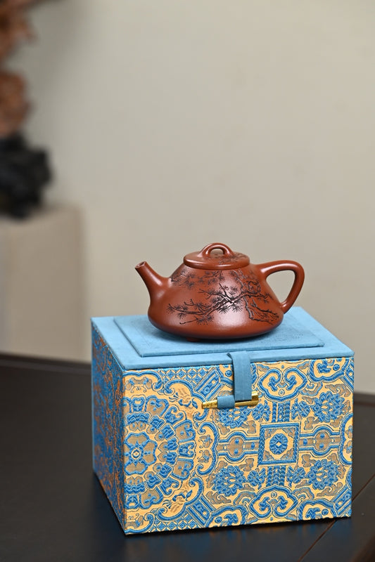 Handmade Yixing purple sand teapot displayed on a decorative blue and gold gift box.