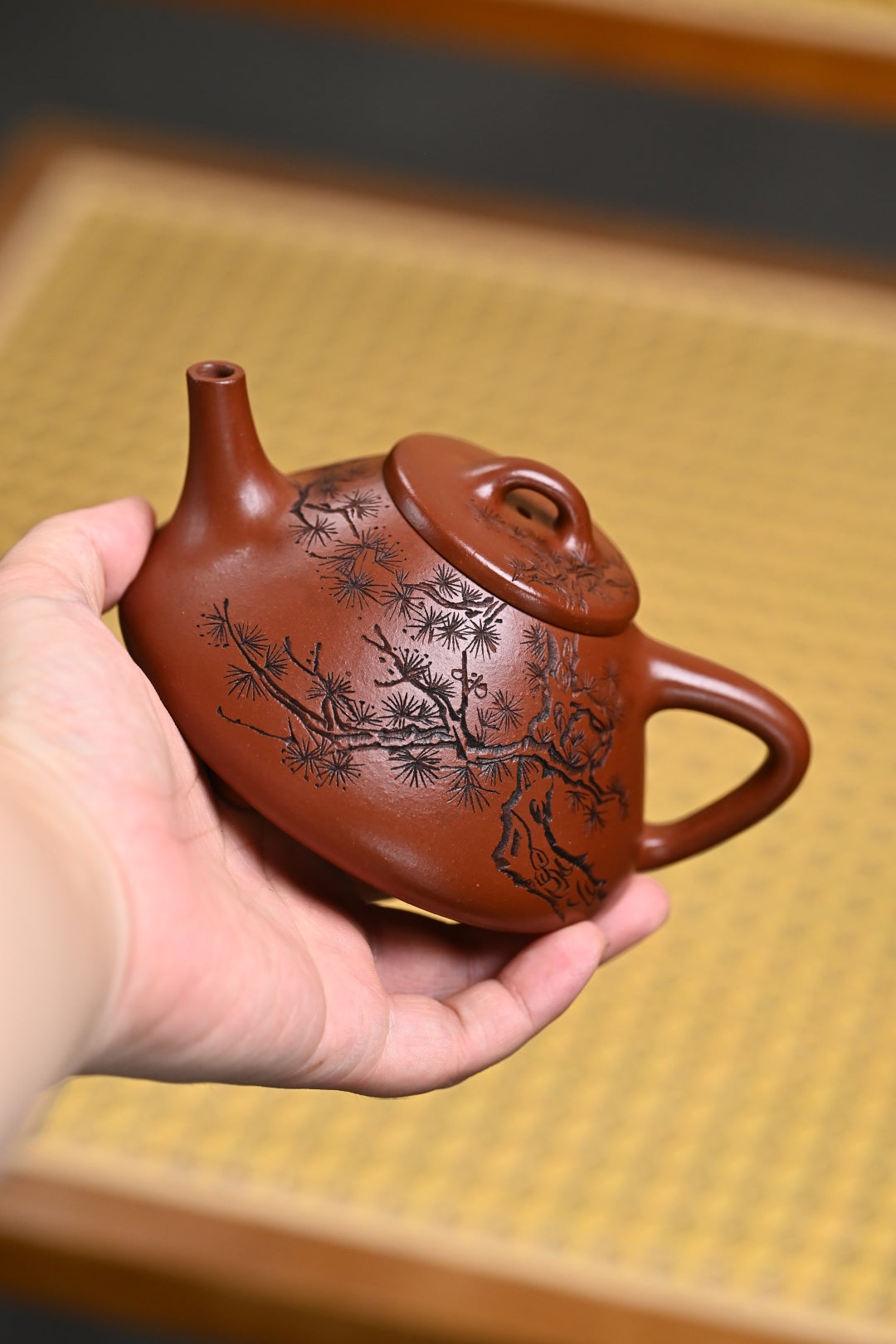 Handmade Yixing purple sand teapot with intricate design, held in hand, showcasing craftsmanship and artistry.